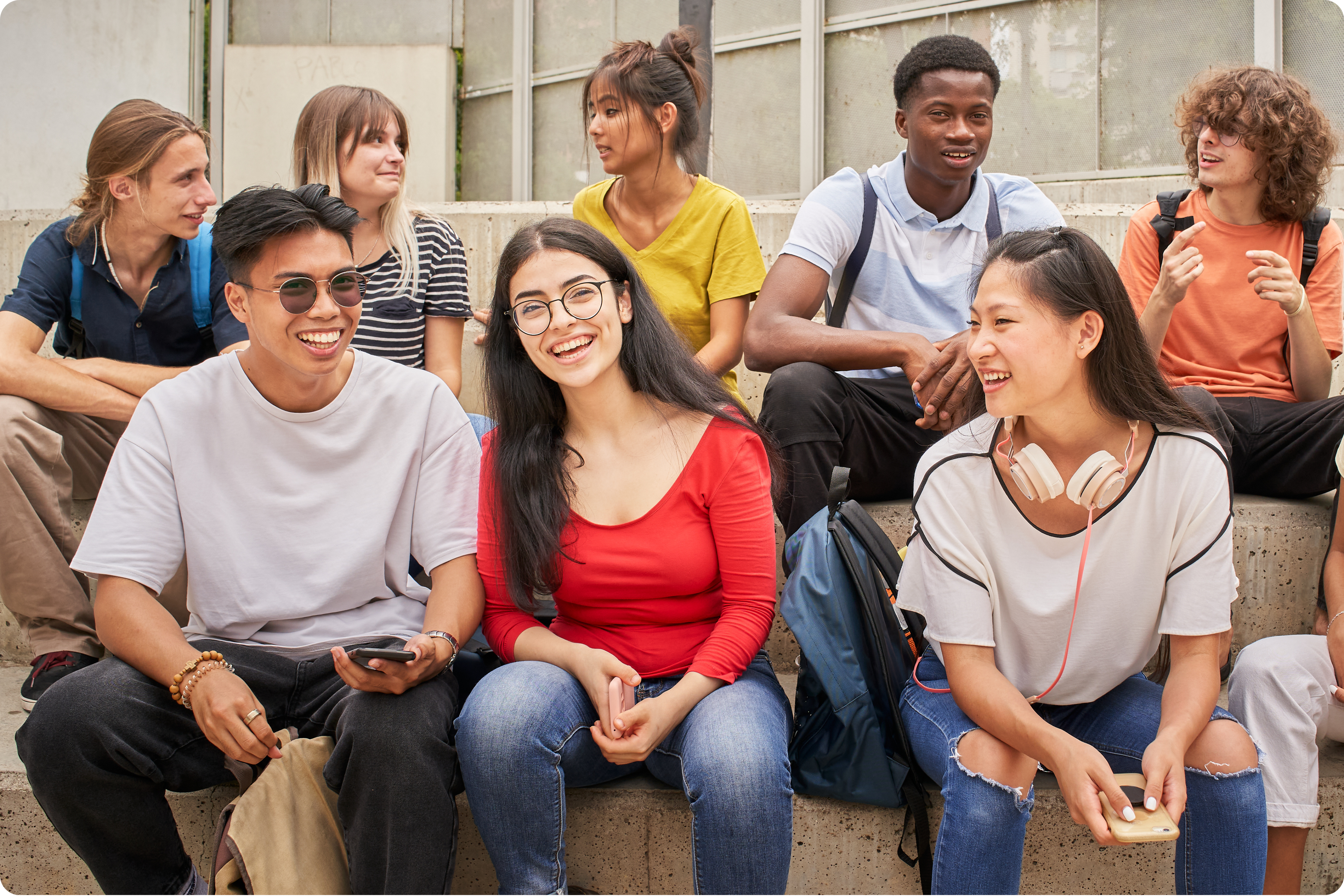 Group of multiracial teens sitting on steps outdoors.