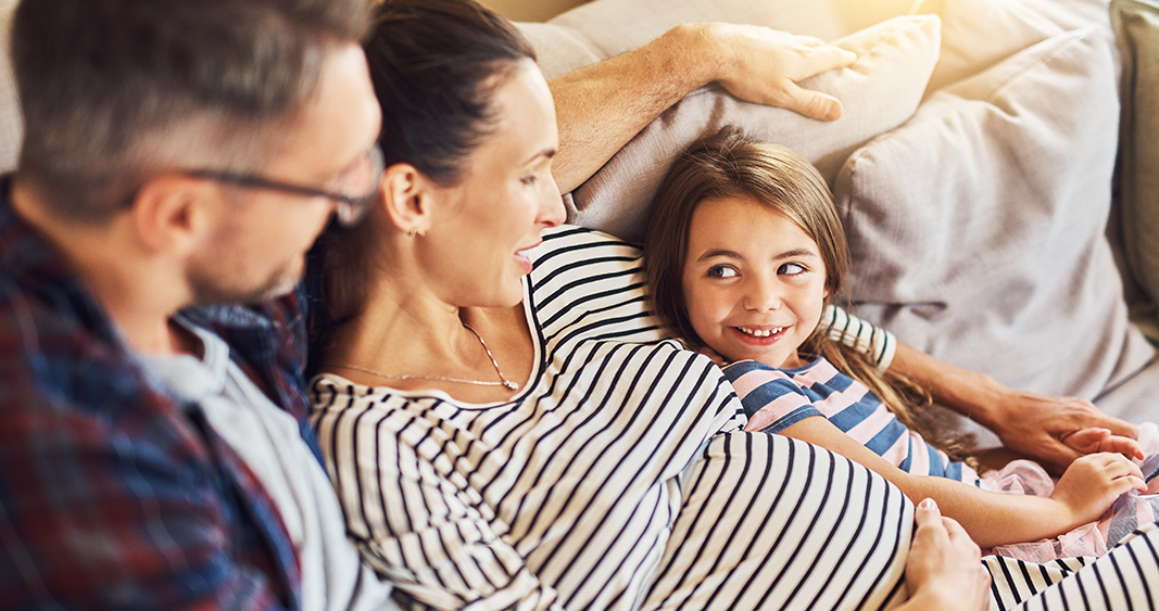 Family husband, pregnant wife and daughter lounging on couch